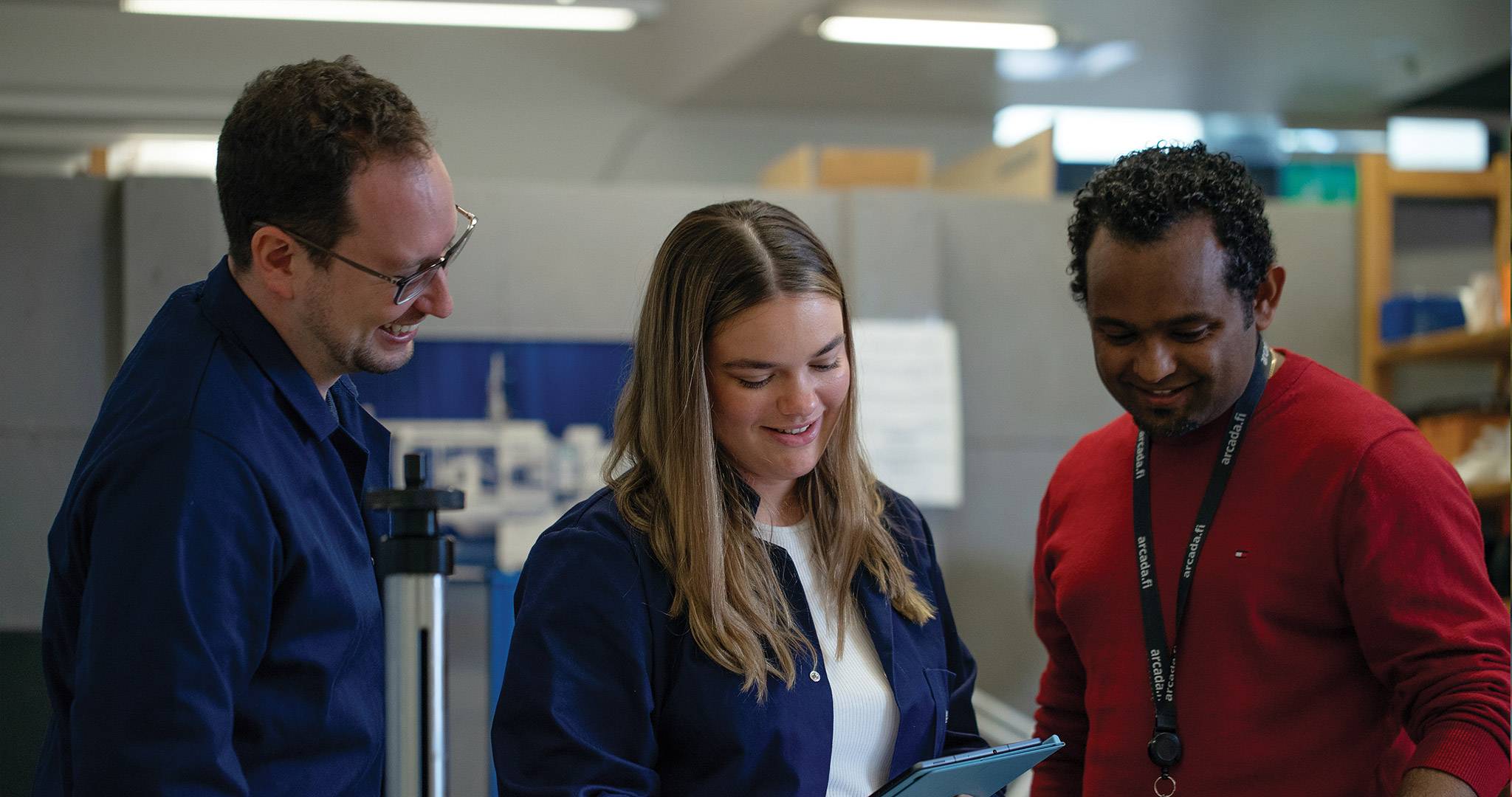 Three people looking down at a tablet.